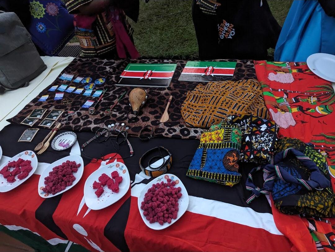 A country table at a cultural night: Kenyan flags, beadwork, a gourd, printed fabrics and plates of snacks